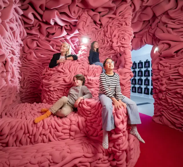 Vier Kinder sitzen auf Schaumstoffgebilden in einer Ausstellung.