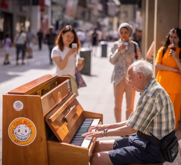 Ein alter Mann spielt Klavier in einer Fußgängerzone. 