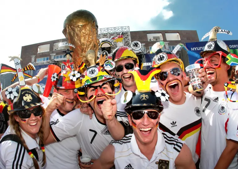 Fußballfans im Deutschland-Trikot und mit schwarz-rot-goldener Bemalung jubeln vor dem Rathaus