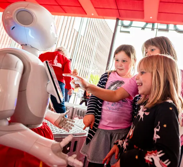 Kinder stehen vor einem Roboter und tippen auf einem Bildschirm.