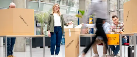 Menschen helfen bei einer Wahl mit, eine junge Dame ist im Vordergrund zu sehen.