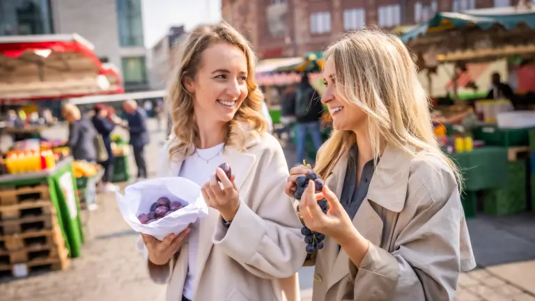 Zwei junge Frauen laufen über den Wochenmarkt auf dem Hansaplatz und essen Trauben