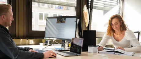 Zwei Personen sitzen in einem Büro und arbeiten am Computer