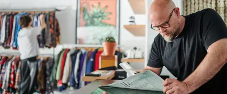 Eine Person steht am Verkaufstresen eines Kleidungsgeschäfts mit einem Steuerbogen in der Hand