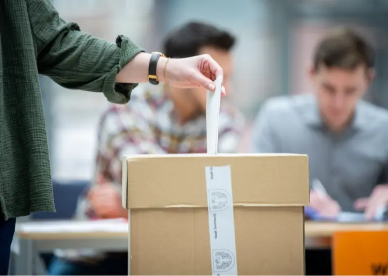 Person wirft einen Stimmzettel in die Wahlurne