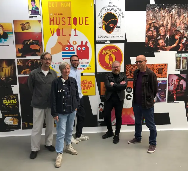 Fünf Personen in der Ausstellung "The music sounds better with you" im Superraum, hinter ihnen an der Wand hängen verschiedene Plakate, die Fotos oder Plattencover zeigen