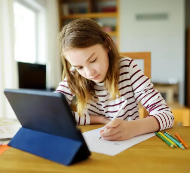 Eine junge Schülerin macht Hausaufgaben mit Tablet und Schreibpapier.