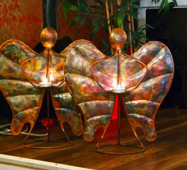Drei Auszeichnungen des "Engels der Nordstadt" nebeneinander, Engelformen aus Metall mit jeweils einem Teelicht-Halter und einem brennenden Teelicht.