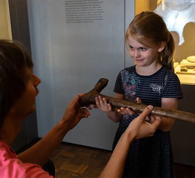 Museumsvermittler übergibt Mädchen ein steinzeitliches Werkzeug