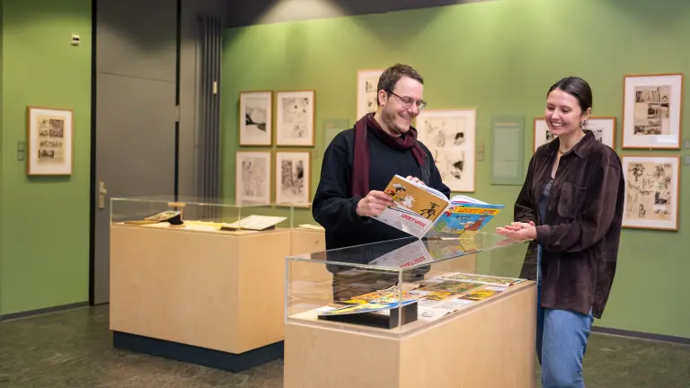 Zwei Personen stehen im Museum und schauen sich lächelnd einen Comic an