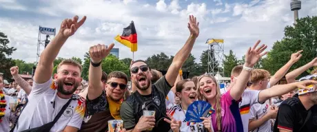 Mehrere jubelnde Fans in Deutschland-Trikots, im Hintergrund Deutschland-Fahnen. 