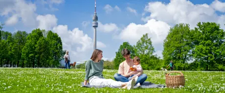 Familie genießt ein Picknick auf einer blühenden Wiese im Westfalenpark Dortmund, mit dem Florianturm im Hintergrund an einem sonnigen Tag.