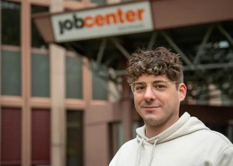 Ein Mann lächelt, im Hintergrund sieht man das Logo des Job Centers