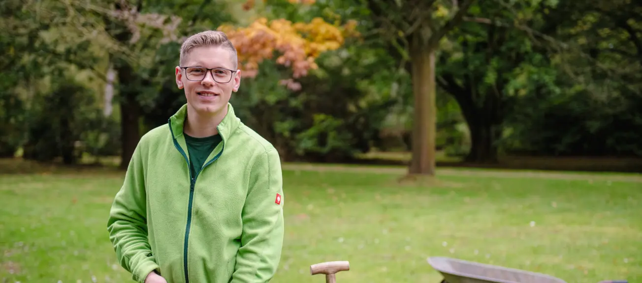 Ein Friedhofsgärtner, welcher mit einer Schaufel ausgestattet in die Kamera schaut.