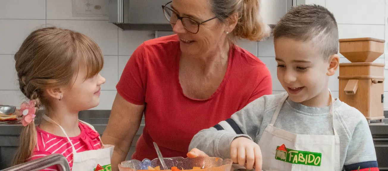 Eine Erzieherin, welche mit zwei kleinen Kindern gemeinsam kocht 