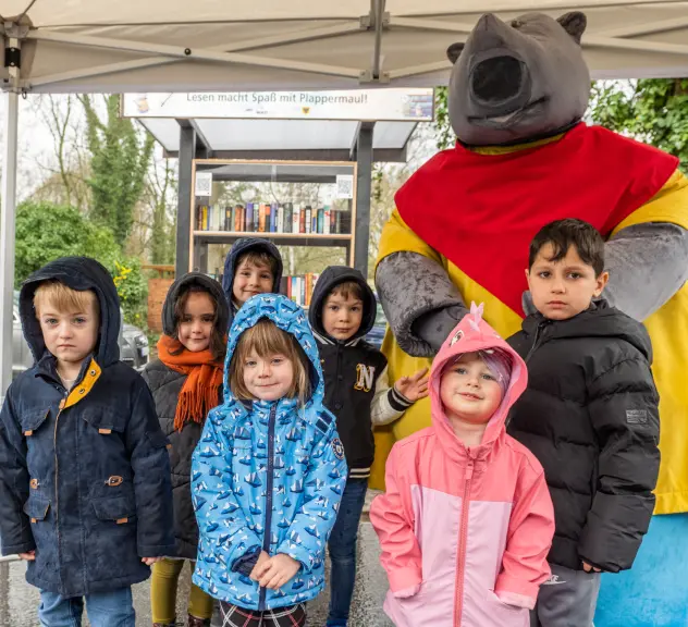 Ein Gruppenfoto von Kindern, im Hintergrund das kostümierte Plappermaul-Maskottchen