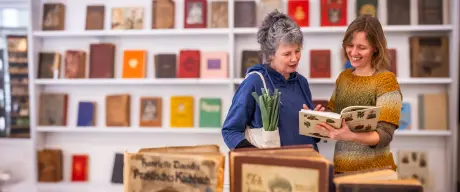 Zwei Frauen schauen lächelnd in ein Buch vor Bücherwand