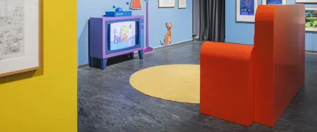 Zu sehen ist ein nachgebautes Wohnzimmer der Simpsons, mit Fernseher und Couch. An den Wänden hängen viele Bilder/Zeichnungen.