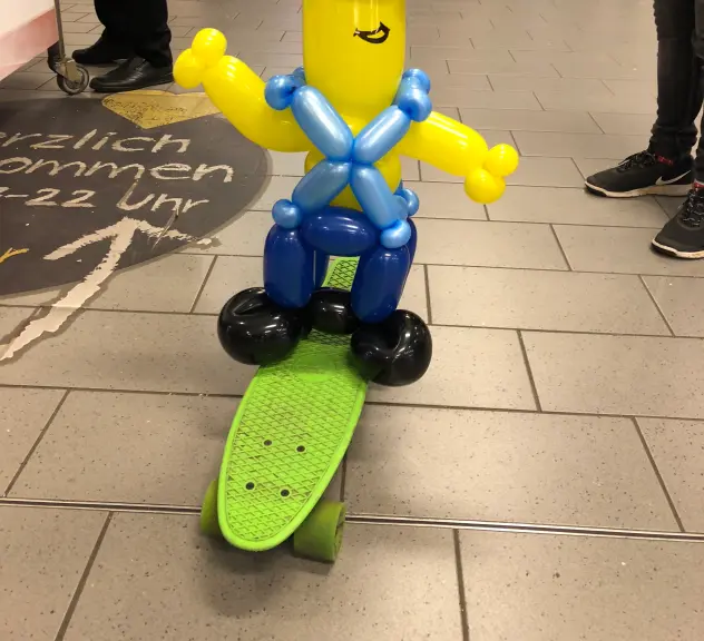 Zu sehen ist eine längliche Minion-Ballonfigur auf einem grünen Skateboard.