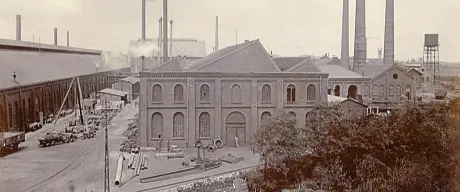 Blick auf das Hoesch-Werk. Im Vordergrund steht ein Fabrikgebäude, im Hintergrund sind viele rauchende Schlote zu sehen.