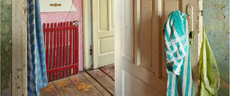 Blick in eine Wohnung, Holzdielen und Türrahmen sind abgesplittert. An der Türklinke hängen bunte Kleidungsstücke. 