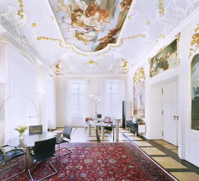 Blick in das Bürgermeisterzimmer von Schwäbisch Hall. Opulentes Dekor an Decke und Wänden. Roter Teppich und kleiner Besprechungstisch im Vordergrund. Hinten großer Schreibtisch.