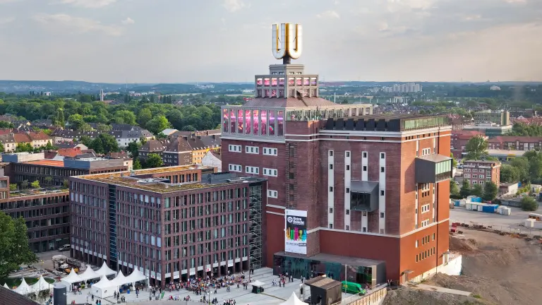 Das Dortmunder U von außen betrachten, dahinter die Stadt Dortmund.