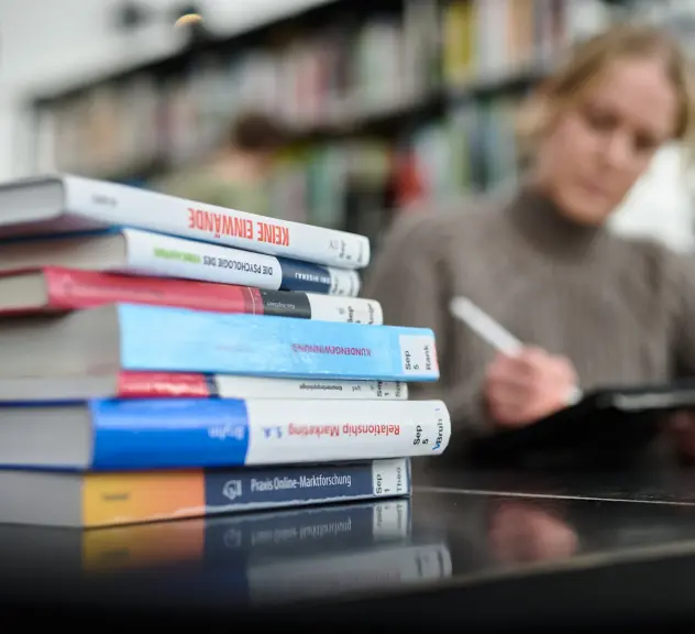 Eine Lernende mit Büchern und IPad am Arbeitsplatz in der Bibliothek