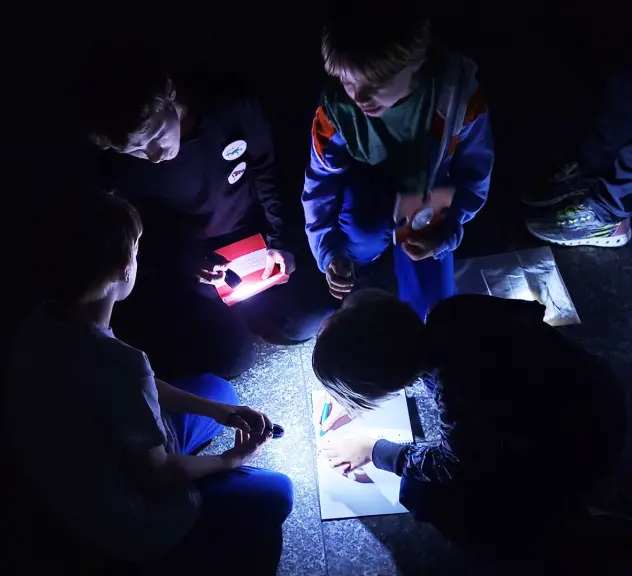 Kinder beleuchten mit einer Taschenlampe ein Stück Papier