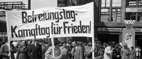 Eine Menschenmenge bei einer Kundgebung, die ein Banner mit der Aufschrift Befreiungstag, Kampftag für Frieden tragen.