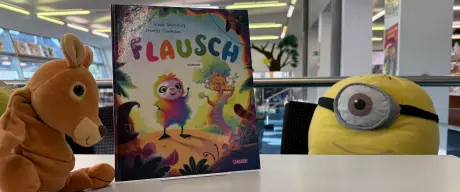 Ein Stofftierkanguruh und ein Minion auf einem Tisch mit dem Buch "Flausch"