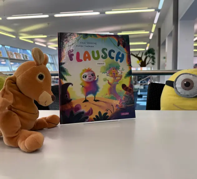 Ein Stofftierkanguruh und ein Minion auf einem Tisch mit dem Buch "Flausch"