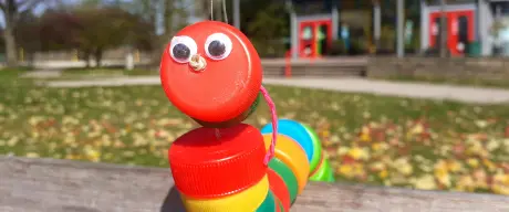 Eine bunte Wurmmarionette aus Deckeln von Plastikflaschen mit aufgeklebten Augen 