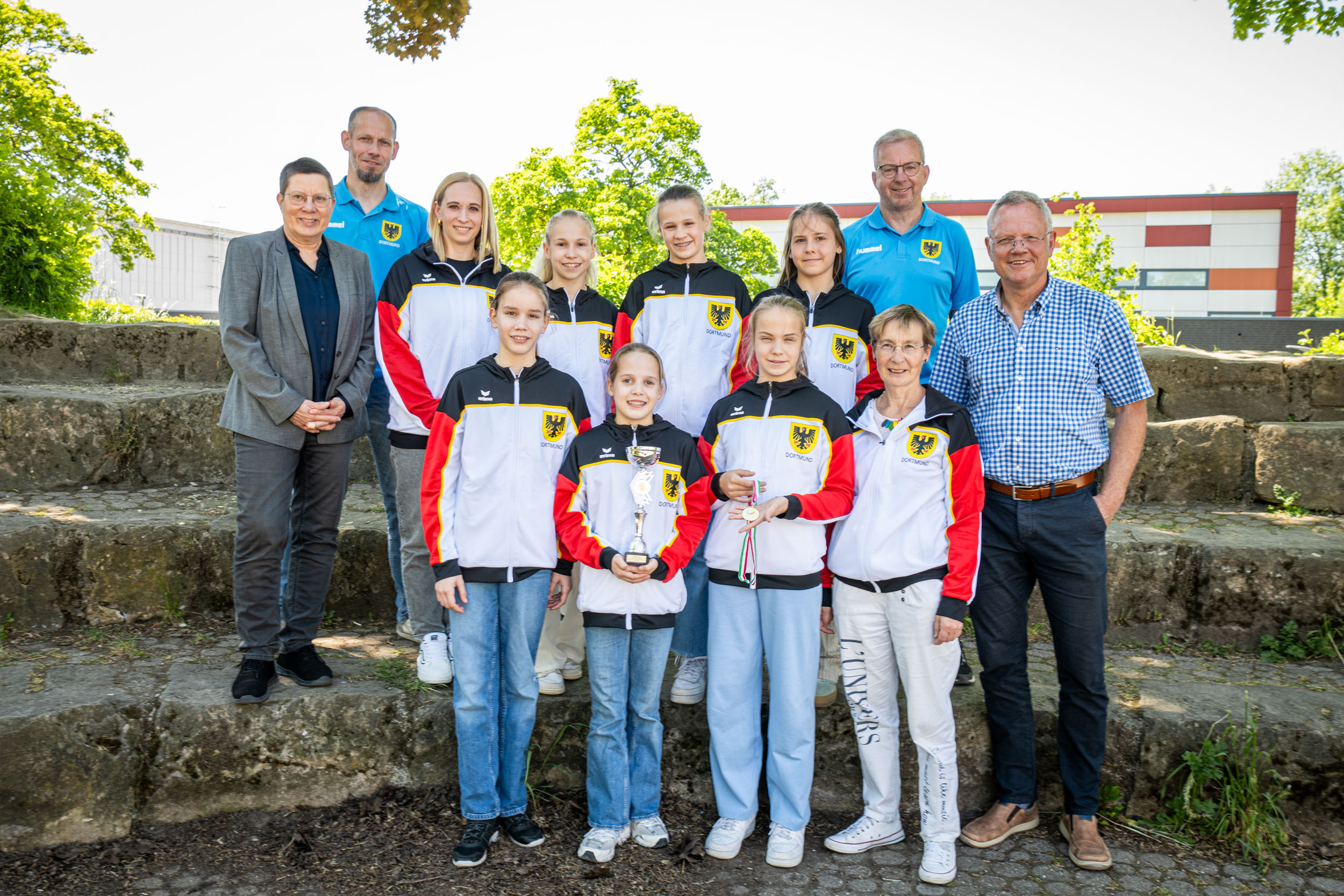 Eine Gruppe von Kindern in Trainingsanzügen steht gemeinsam mit Dezernentin Birgit Zoerner und weiteren Personen auf einer Treppe und schaut in die Kamera.