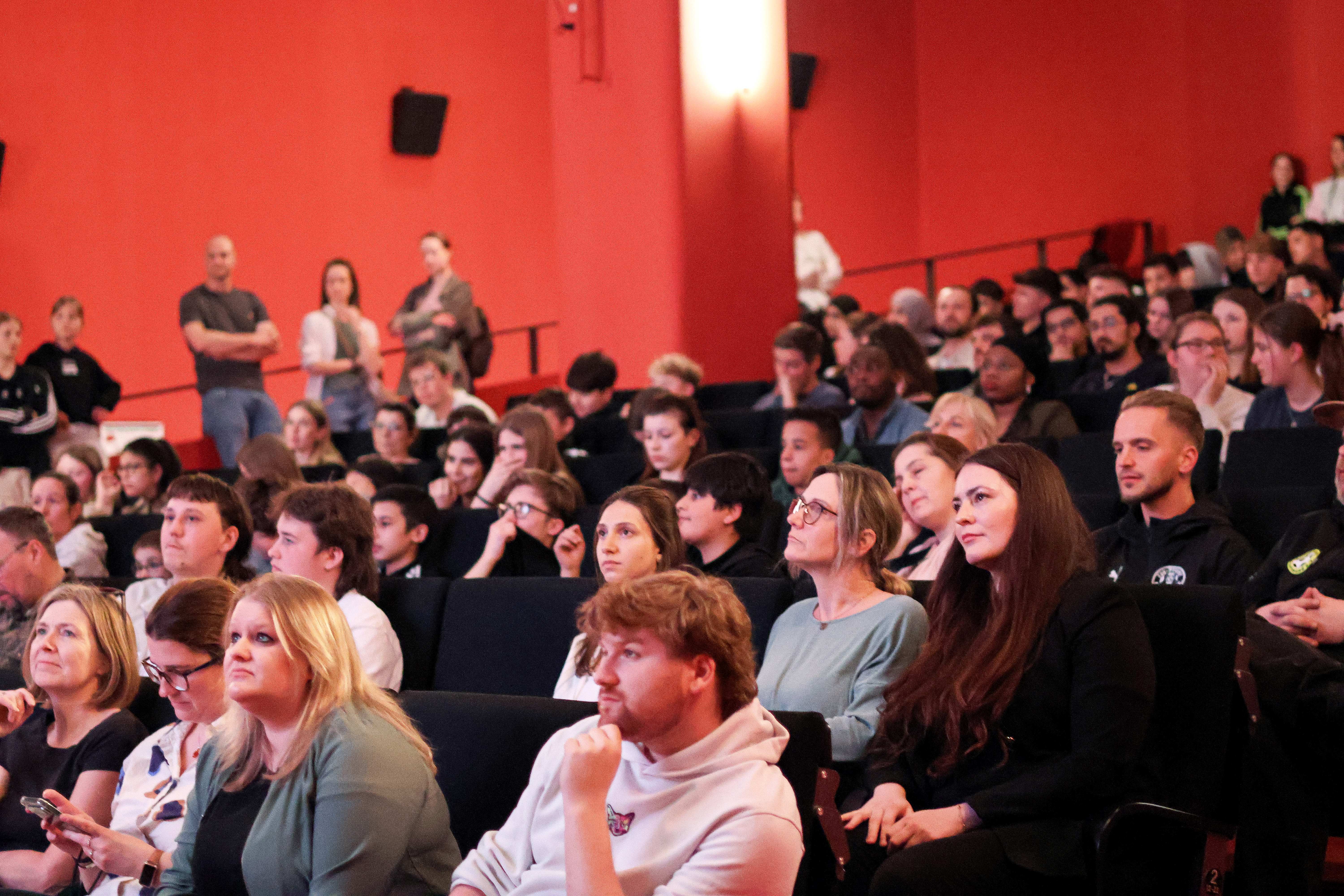 Viele junge Menschen sitzen in einem Saal und hören gespannt einem Vortrag zu.